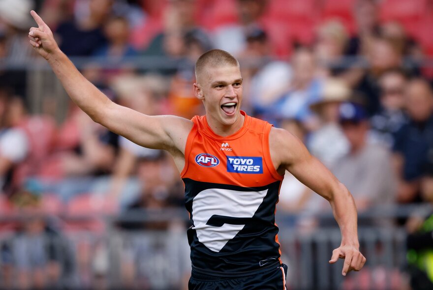 A GWS Giants player holding a hand in the air and sticking his tongue out during a match. 