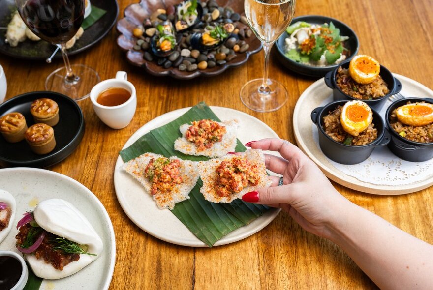 A hand selecting a small savoury snack, from one of several carefully arranged dishes of food on a restaurant dining table.