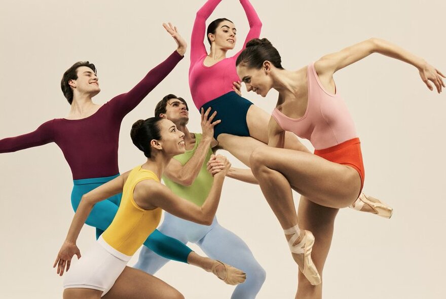 Five ballet dancers in a group pose, all in different positions and dressed in vibrant, contrasting dancewear.