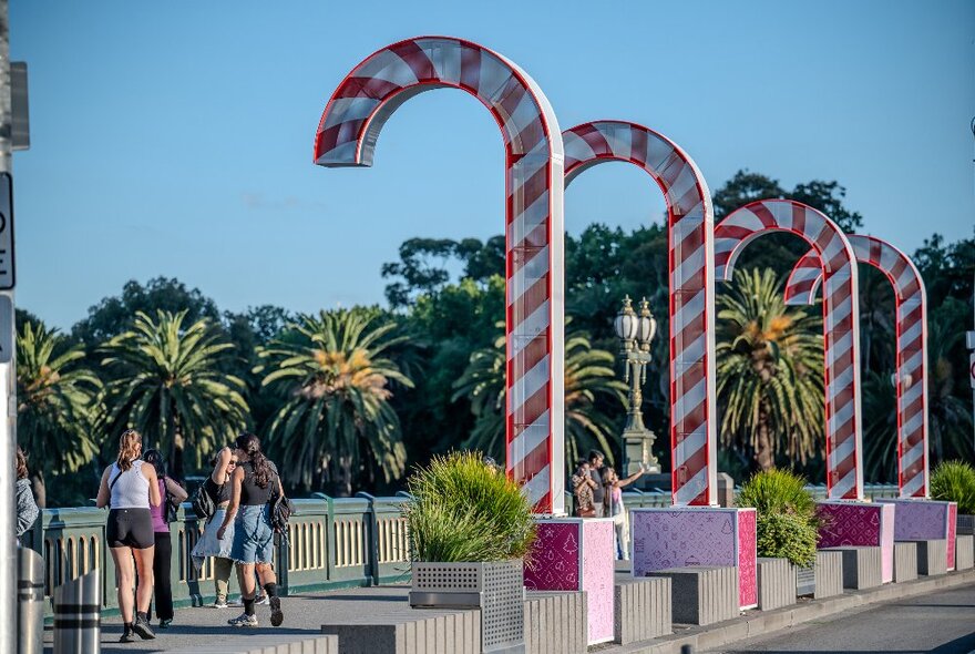 People walk by a set of giant red and white striped candy canes on Princes Bridge