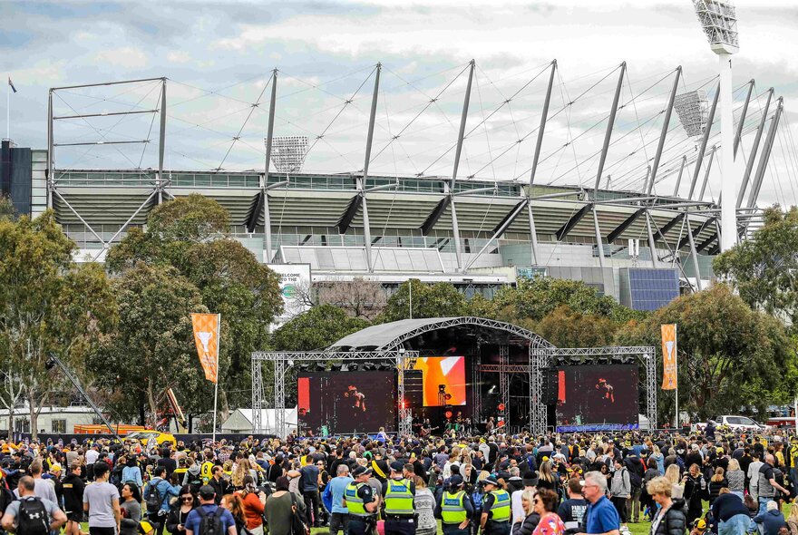 A crowd of people watching something on an outdoor stage out the front of the MCG in Melbourne.