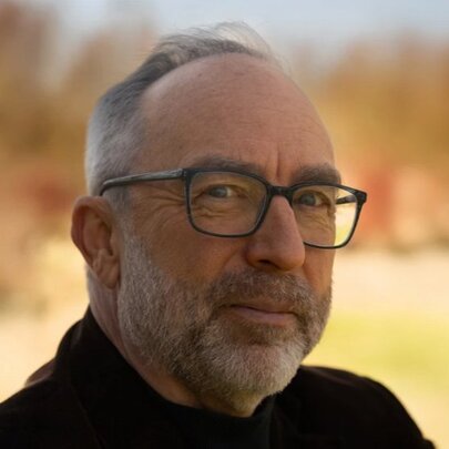 Wikipedia founder, Jimmy Wales, slightly smiling for a portrait with a bright but blurred lanscape in the background.