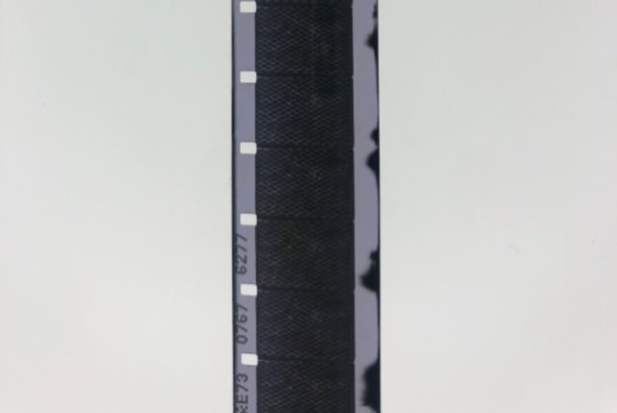 An almost black strip of 16mm film against a white background.