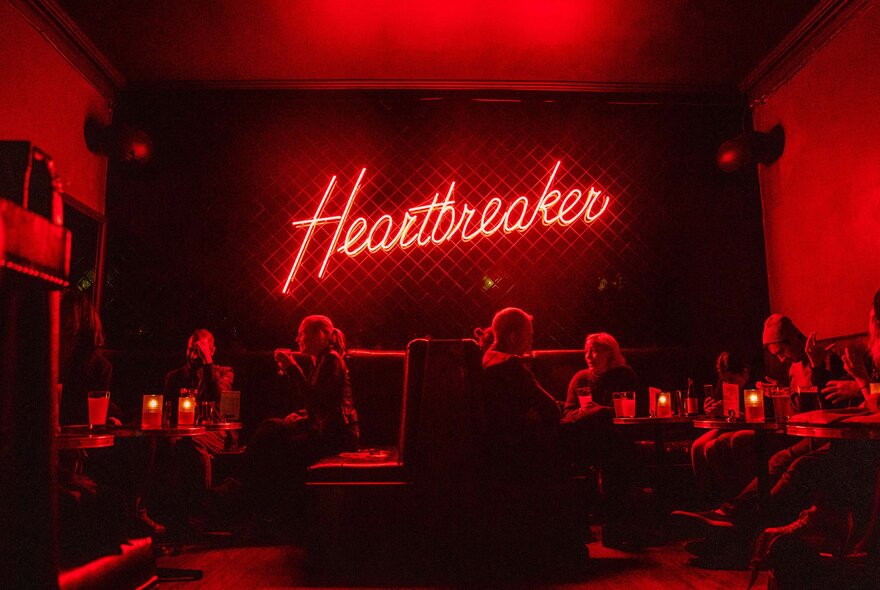 The darkened interior of a bar, lit up only by a red neon sign.