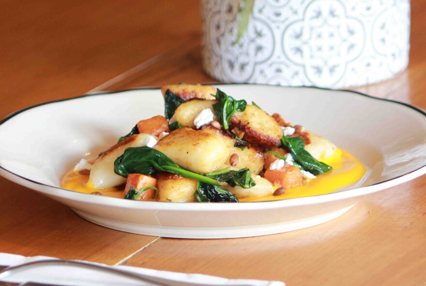 A plate of gnocchi with spinach and pine nuts in it