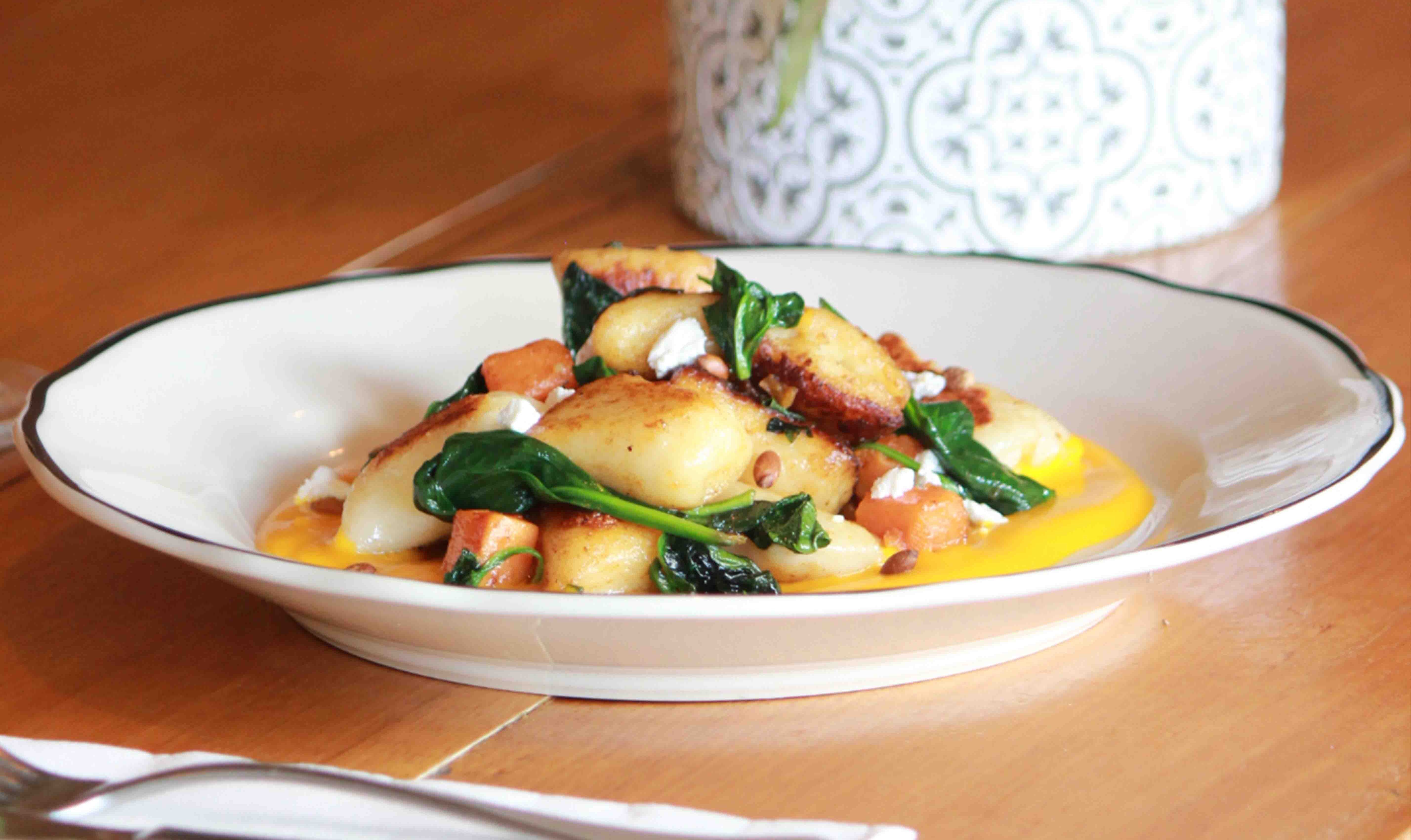 A plate of gnocchi with spinach and pine nuts in it