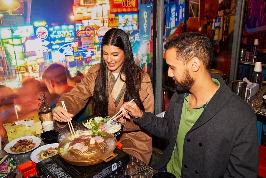 Two people cooking meat on a hot pot