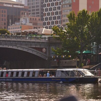Cruise boat on Yarra River with buildings and bridge.