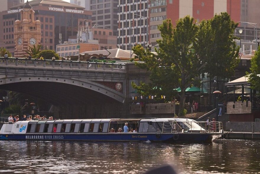 Cruise boat on Yarra River with buildings and bridge.
