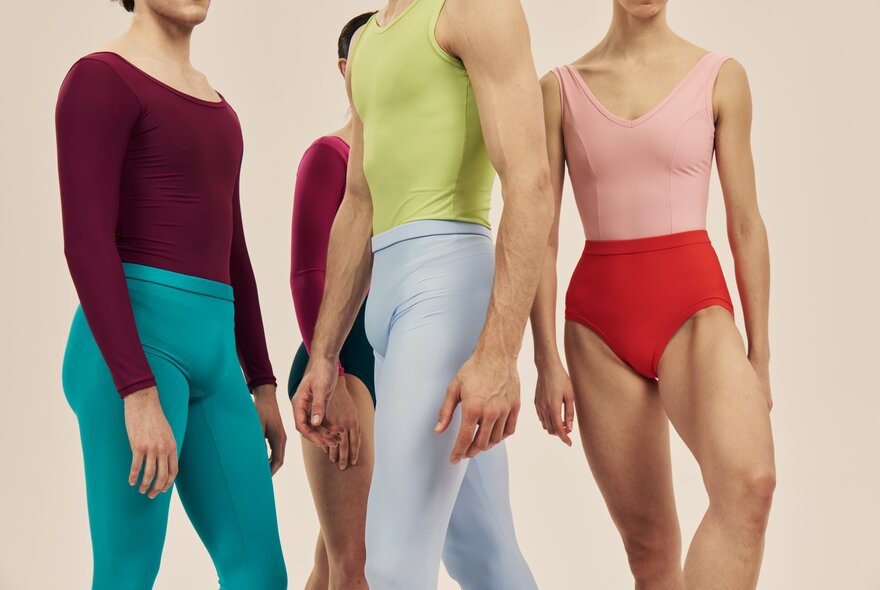 Four ballet dancers in a group pose, their heads and lowers legs out of the frame, all dressed in vibrant, contrasting dancewear.