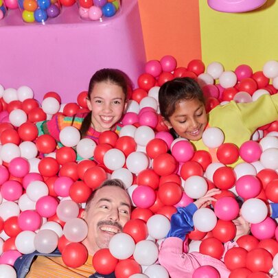 Two kids and a dad in a pink ballpit.