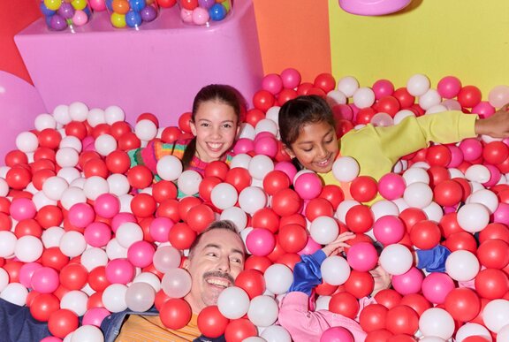 Two kids and a dad in a pink ballpit.