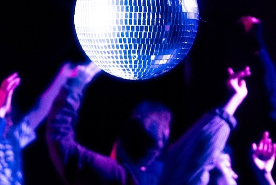 Revellers in a darkened nightclub with a large disco ball above them.