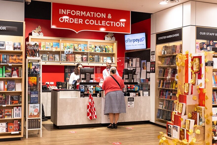 A person at the information counter at Dymocks Melbourne with staff assisting and bookshelves all around. 