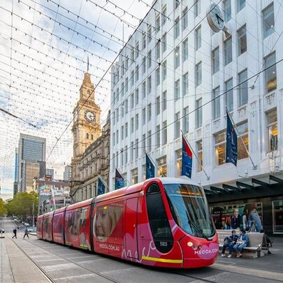 Melbourne's Bourke St Mall with a red tram in the centre, buildings on either side and pedestrians walking around.