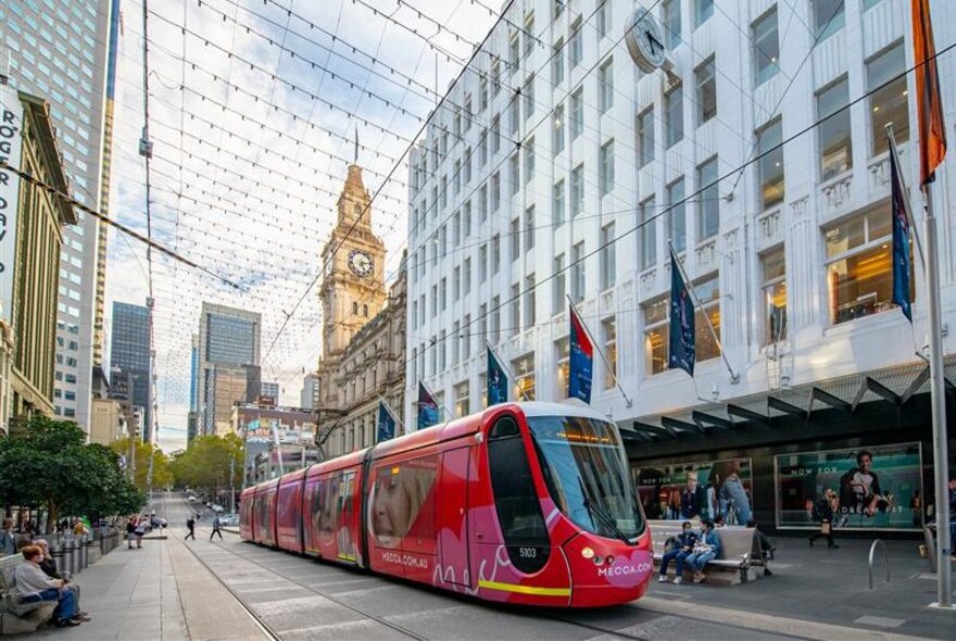 Melbourne's Bourke St Mall with a red tram in the centre, buildings on either side and pedestrians walking around.