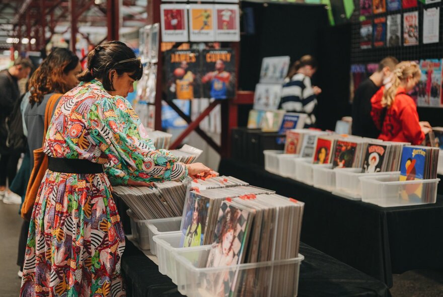 Person browing vinyl LPs in plastic boxes in a market setting.