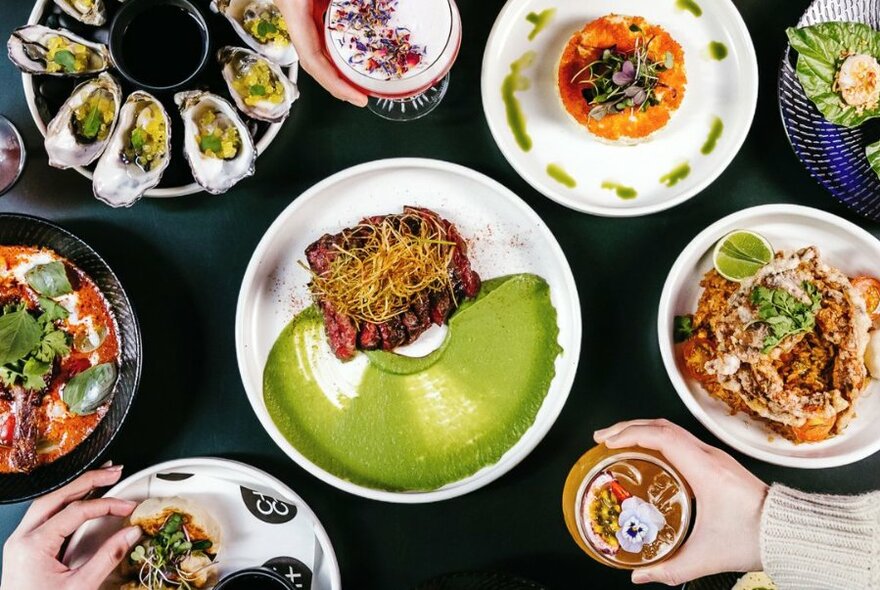 Overhead shot of dishes on a table, with hands holding drinks.