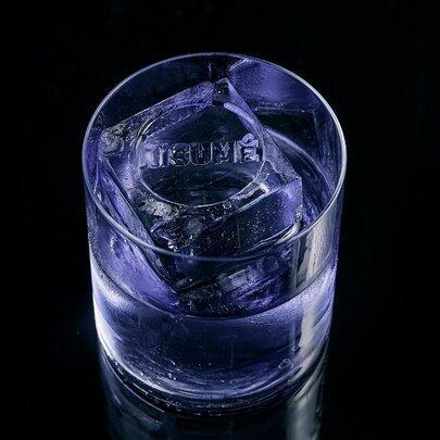 A cocktail in a glass with an ice cube that says Kisume.