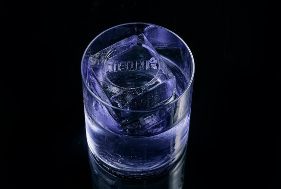 A cocktail in a glass with an ice cube that says Kisume.