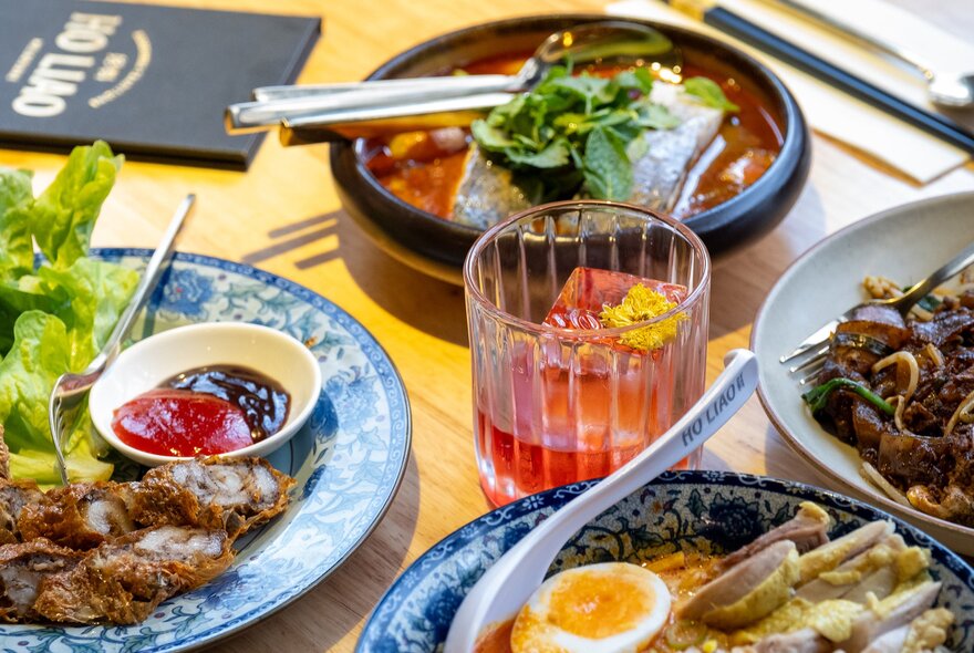 A table with Malaysian food on it including laksa, fish and pork dishes.