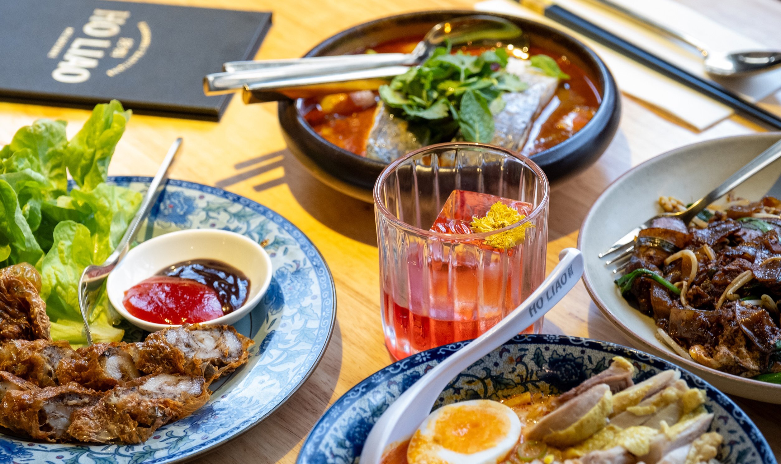 A table with Malaysian food on it including laksa, fish and pork dishes.