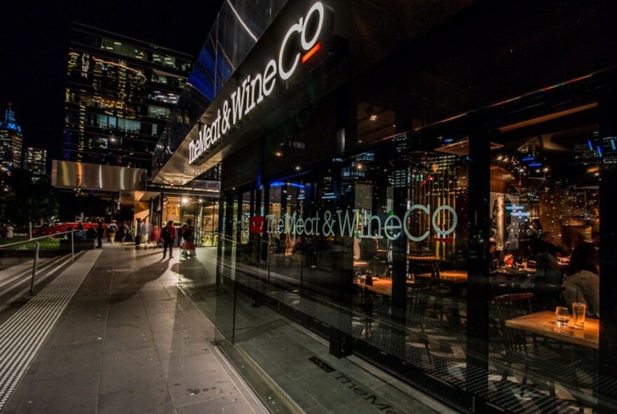 Shopfront of The Meat & Wine Co restaurant at night.