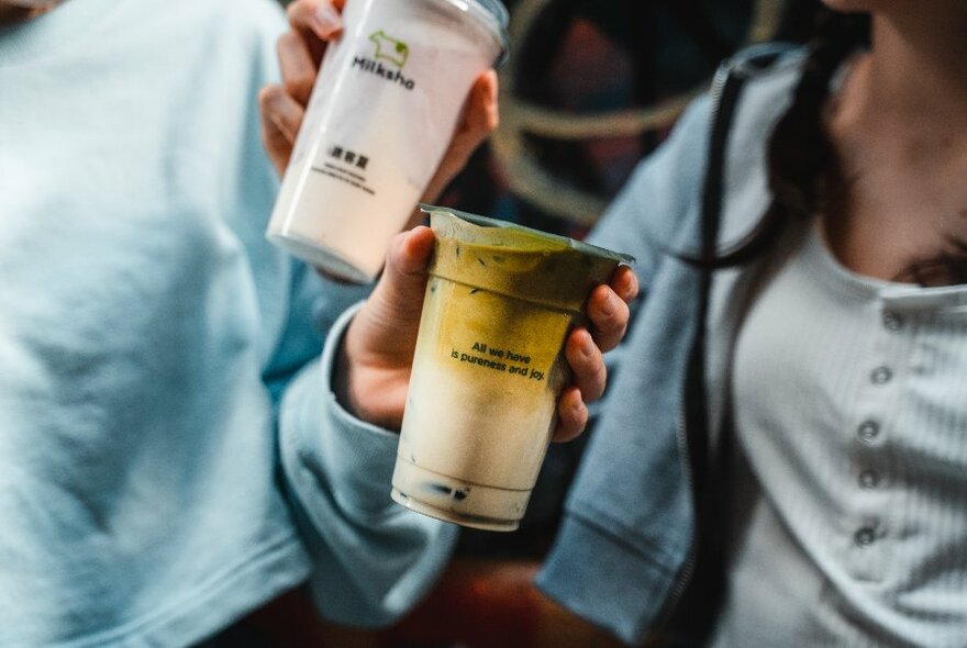 Two people showing off their bubble teas. 