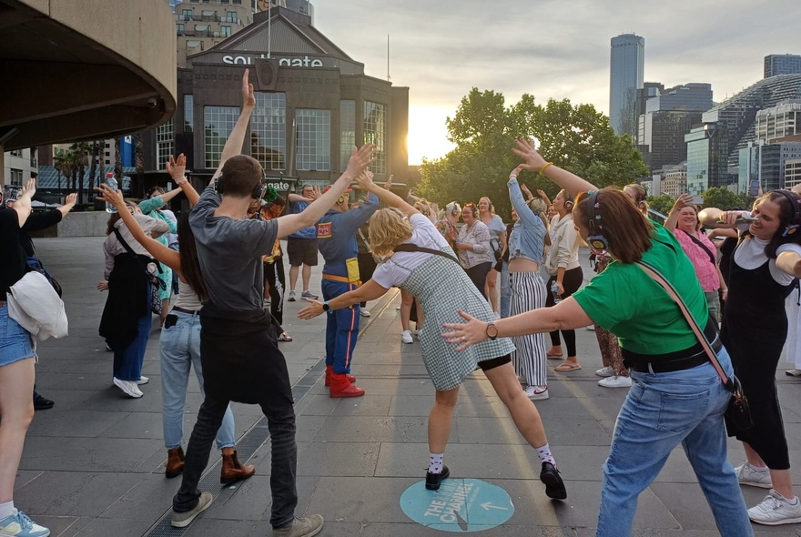 A silent disco group in various dance poses in the middle of the city at dusk.