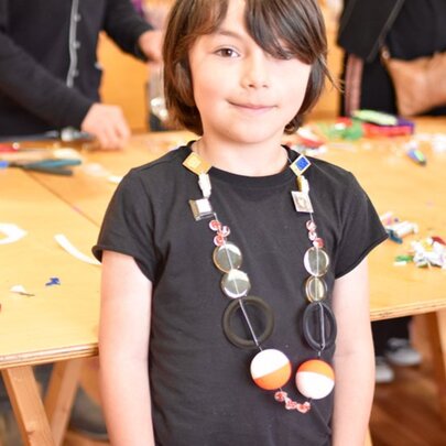A child wearing a handmade necklace created using recycled and upcycled materials during an art workshop. 