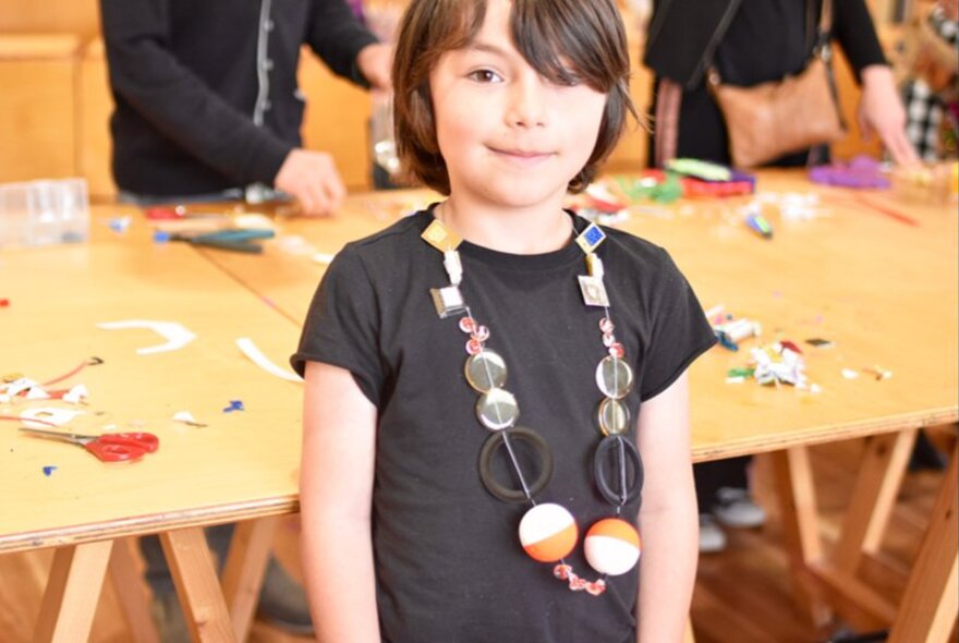 A child wearing a handmade necklace created using recycled and upcycled materials during an art workshop. 