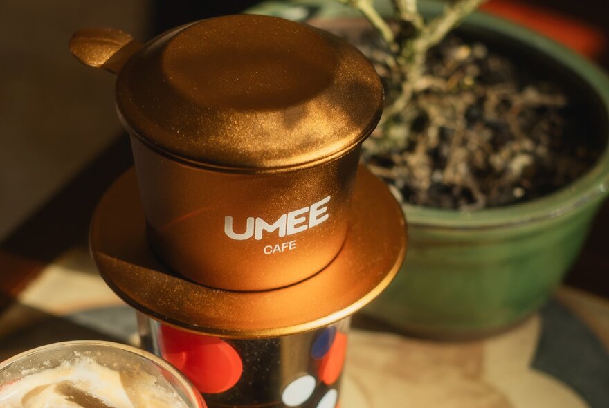 A single-serve drip brewer used to make coffee directly into a cup, with UMEE cafe branding on the filter section.