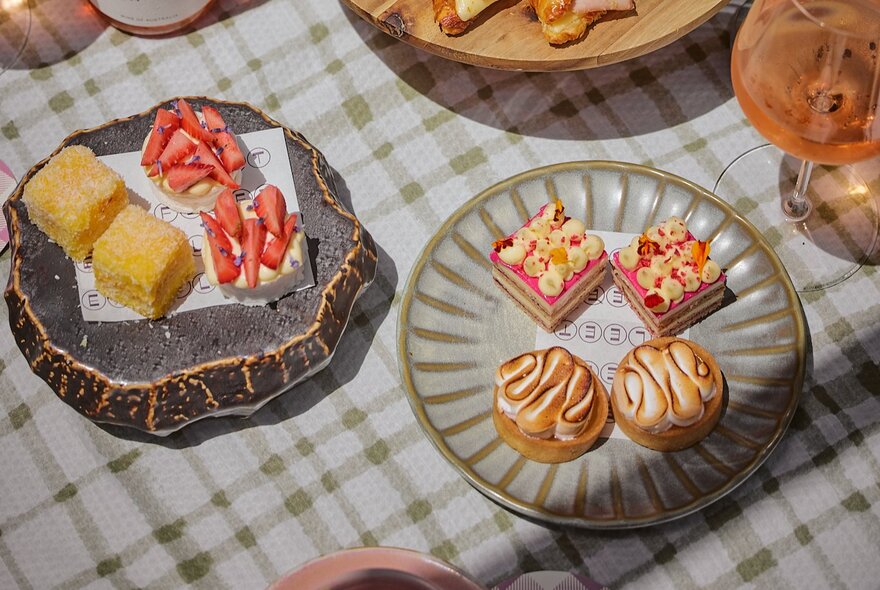 High Tea plates with small cakes and savoury snacks on a checked tablecloth. 