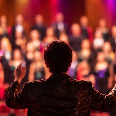 Looking at the back of a man conducting an out-of-focus choir. 