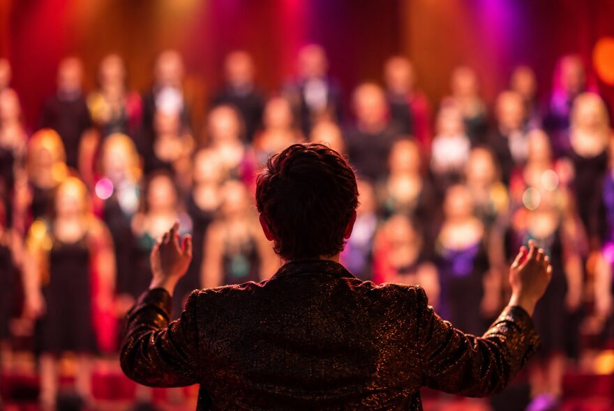 Looking at the back of a man conducting an out-of-focus choir. 
