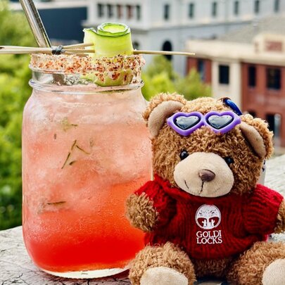 Toy bear and jamjar cocktail on a ledge overlooking buildings.