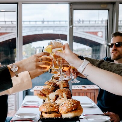 People on a long table all clinking glasses in a toast on a boat. 