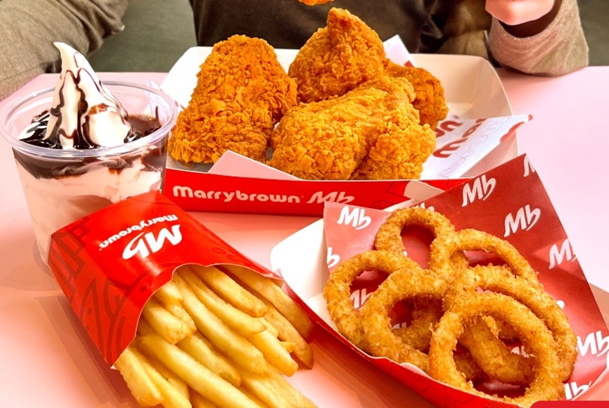 Fried chicken, fries, onion rings and an ice-cream sundae in red Marrybrown branded cardboard takeaway containers.