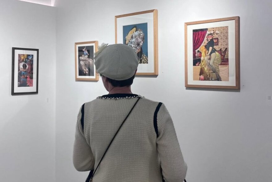 Person looking at framed artworks on a white gallery wall.
