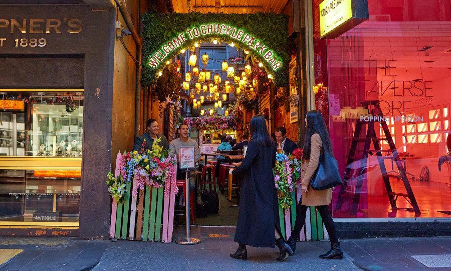 Two women entering a colourful laneway bar.