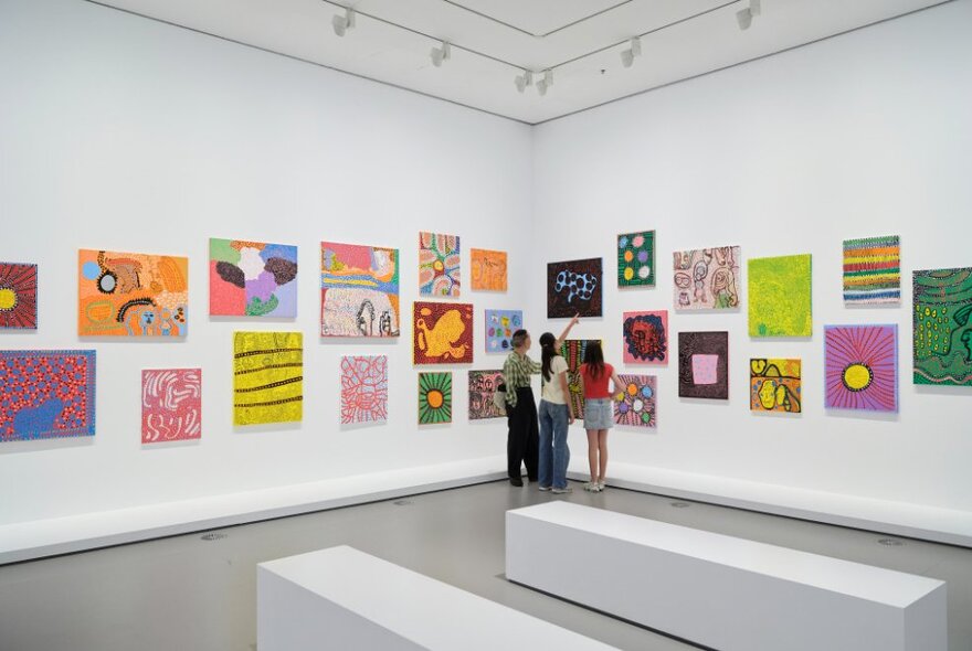 A group of teens looking at an exhibition of colourful artworks on display in a gallery.