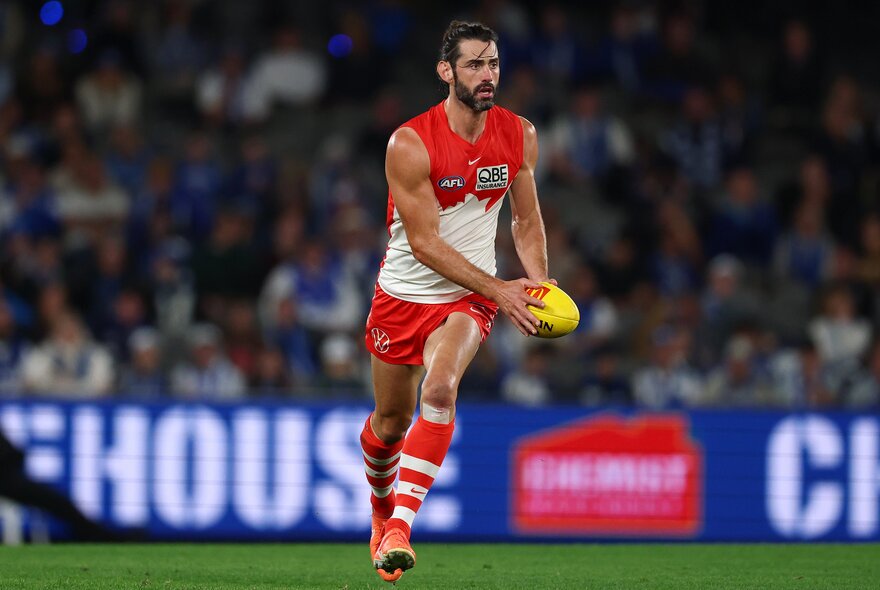 Sydney Swans AFL football player running on the field holding the ball during a match.