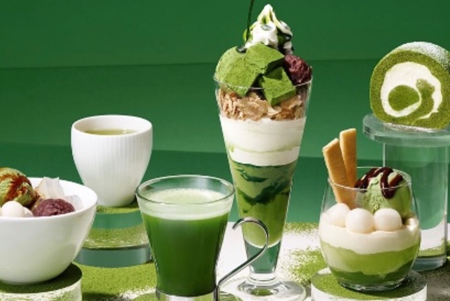 A display of green and white matcha-flavoured products including teas and desserts, arranged in clear glasses on a table against a green background.