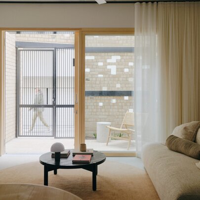 A thoughtfully designed living room interior from the 'Two Sisters' project, with a large window, soft sheer curtains, and lounge room furniture.