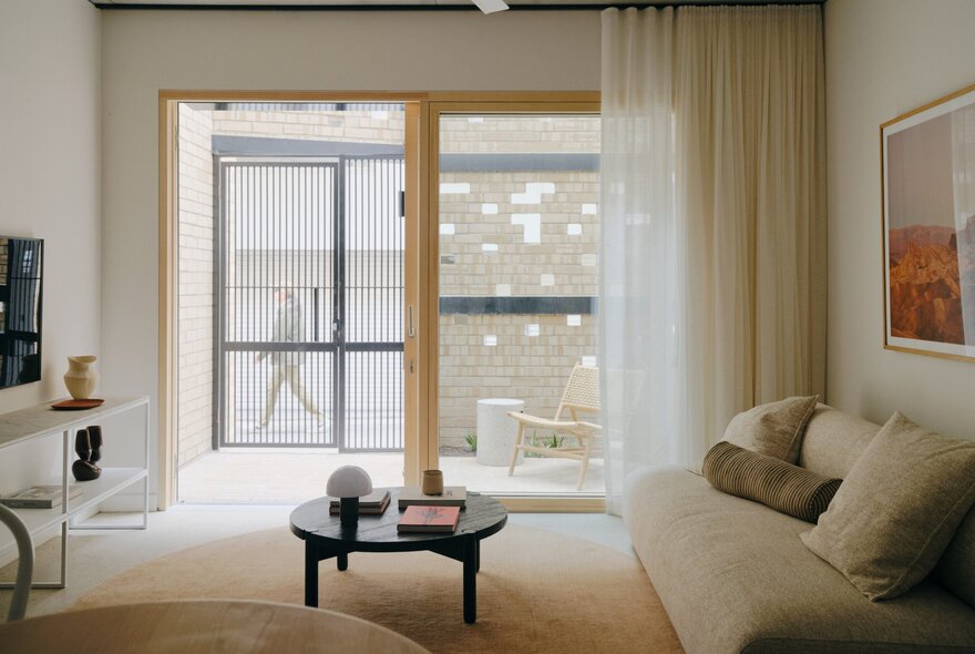 A thoughtfully designed living room interior from the 'Two Sisters' project, with a large window, soft sheer curtains, and lounge room furniture.