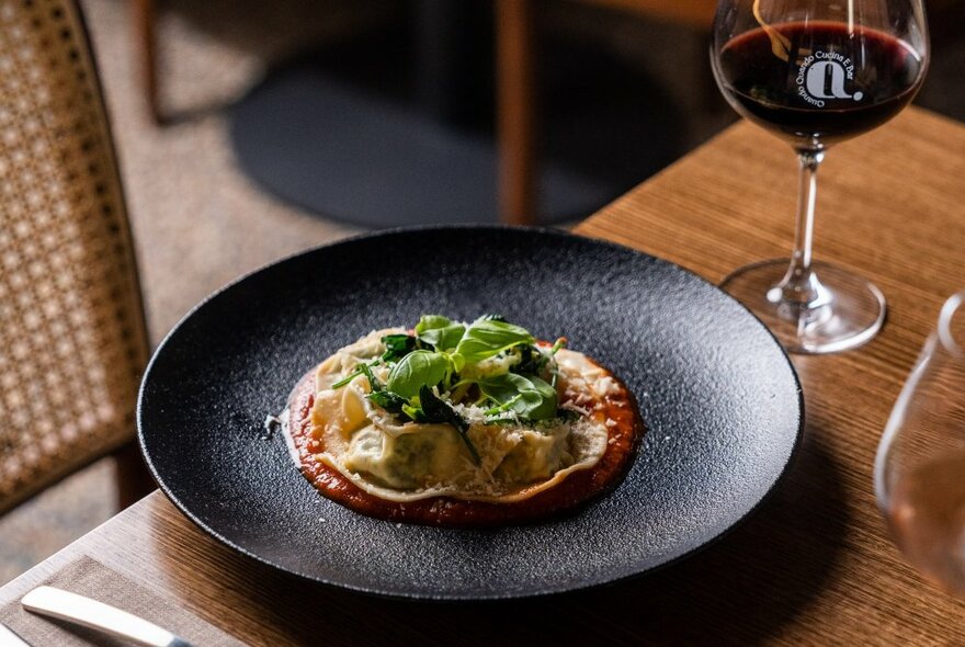 Italian pasta dish with garnish and parmesan on a black plate with a glass of red wine.