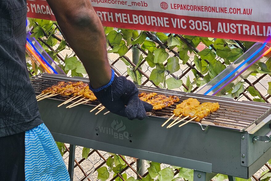 Hands of a cook making satays outside on a grill. 