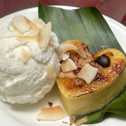 A heart-shaped crème brûlée resting on a banana leaf next to a large scoop of vanilla ice cream, garnished with flaked almonds.