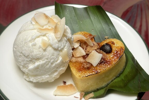 A heart-shaped crème brûlée resting on a banana leaf next to a large scoop of vanilla ice cream, garnished with flaked almonds.