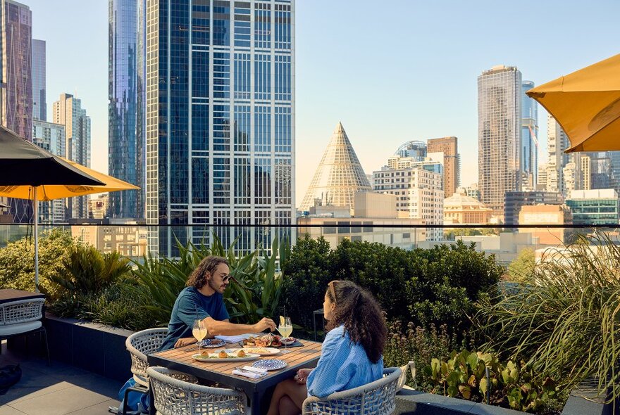 A couple dining on share plates on a rooftop overlooking the city skyline.